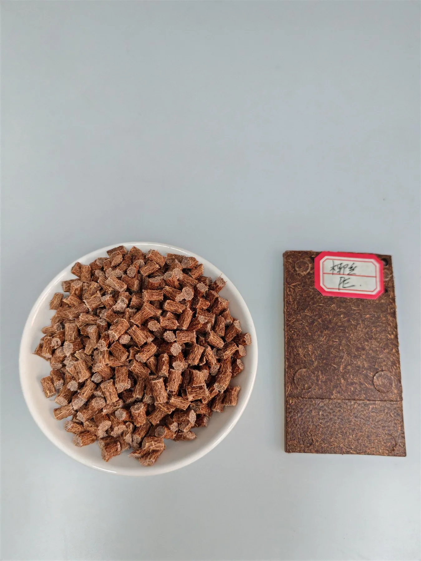 Coconut fiber PE masterbatch pellets in a dish beside a molded sample plaque